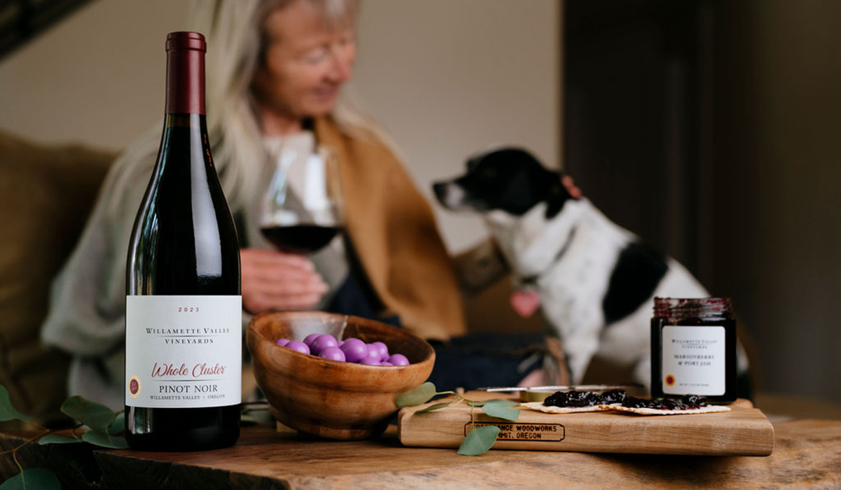 A bottle of Whole CLuster Pinot Noir on a table with a woman and her dog in the background.